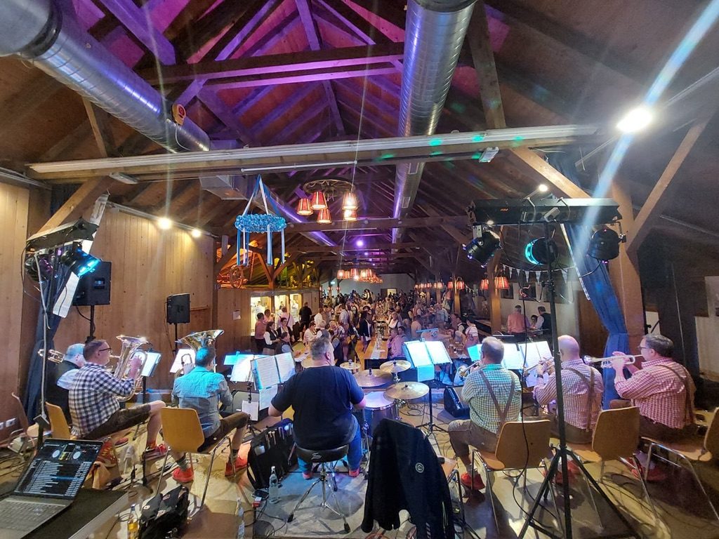 blech'n'takt live in einer Festhalle: Combo auf der Bühne, davor das tanzende Publikum unter pinkem Bühnenlicht.