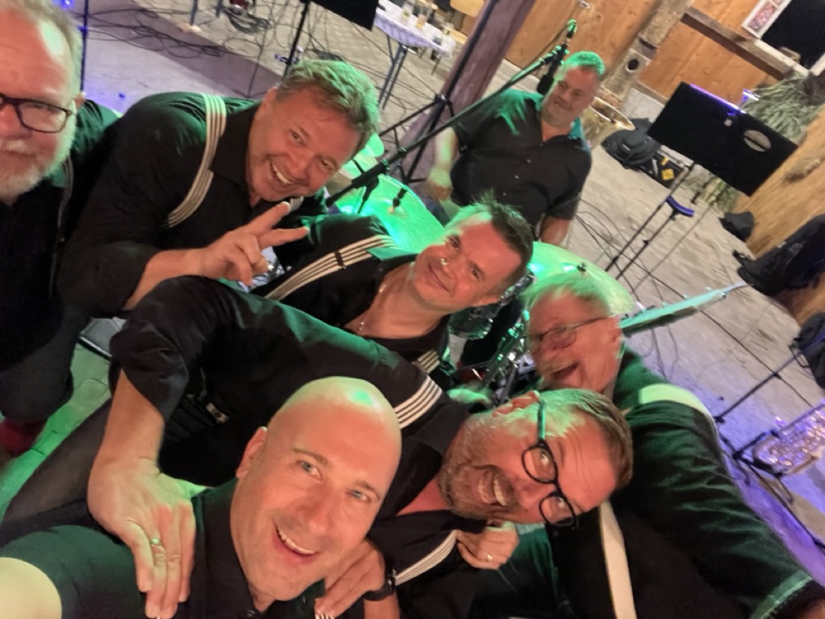 Selfie der Combo nach einem Auftritt, alle lachen, grünes Bühnenlicht im Hintergrund.