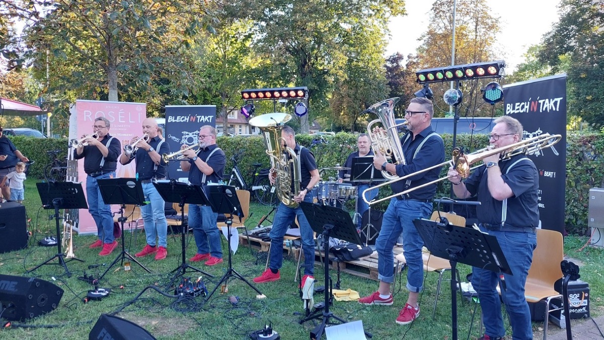 Open-Air-Auftritt im Park: die ganze Combo mit Trompeten, Posaune, Tuba unter dem BLECH'N'TAKT-Banner.